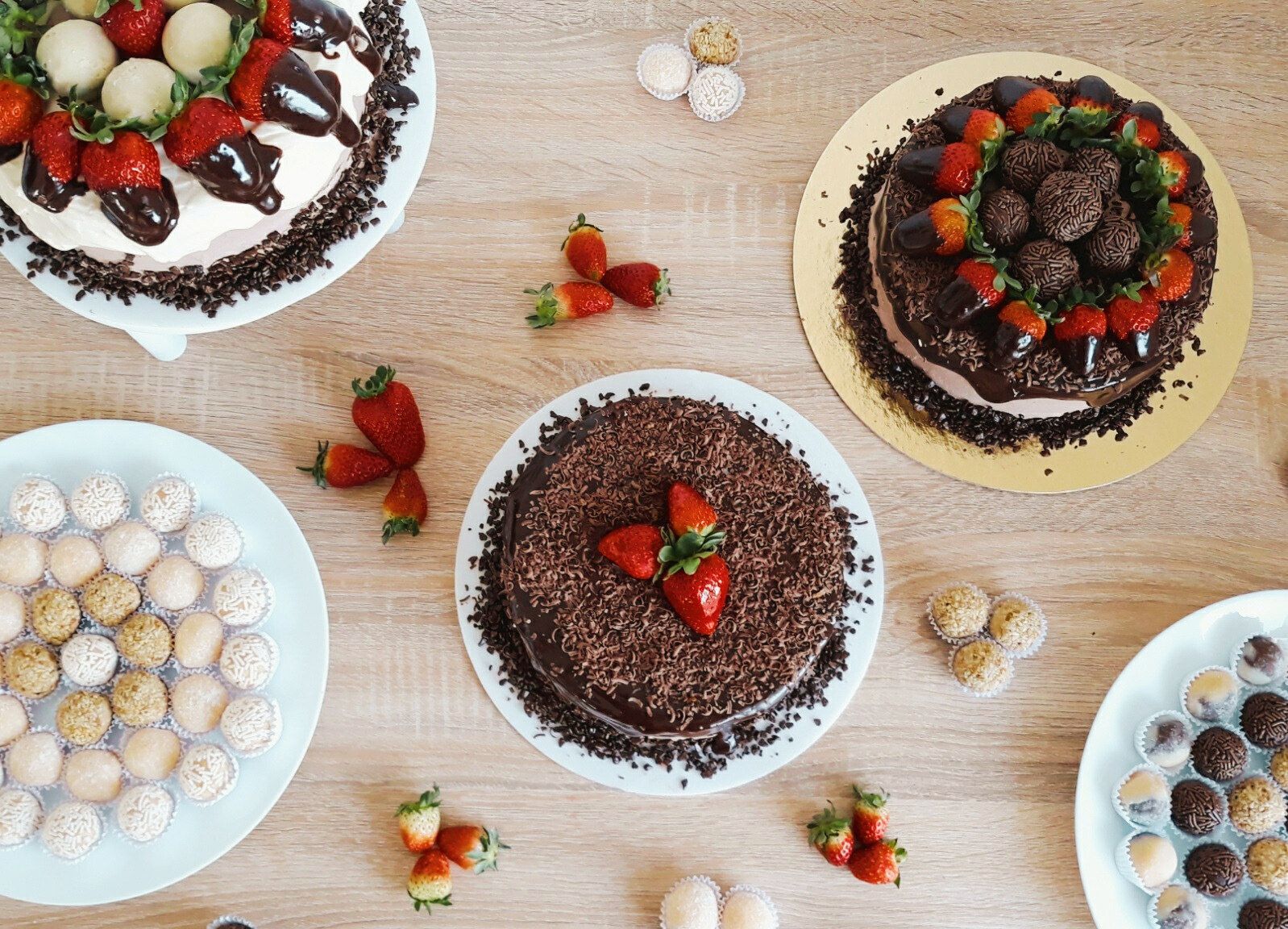 Mesa vista de cima com tortas decoradas com morangos e chocolate e pratos de brigadeiros